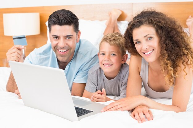 Uśmiechnięty młody rodzinny używać laptop robić zakupy online wpólnie na łóżku