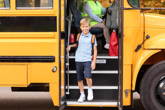 Zdjęcie uśmiechnięty nastolatek wysiada z żółtego autobusu szkolnego.