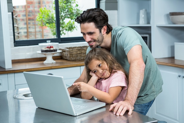 Uśmiechnięty ojciec i córka używa laptop w kuchni