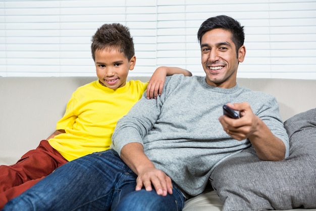 Uśmiechnięty ojciec i syn ogląda tv na kanapie