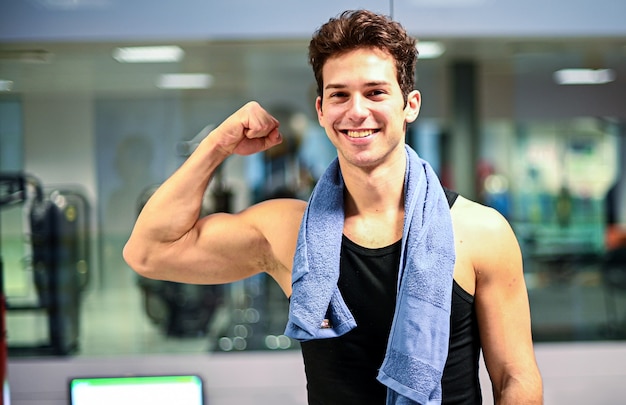 Uśmiechnięty osobisty trener w gym pokazuje jego bicepsy