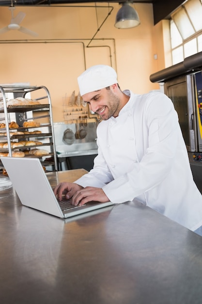 Uśmiechnięty piekarz używa laptop na worktop