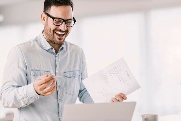 Uśmiechnięty przedsiębiorca z papierami na spotkaniu online z współpracownikami na laptopie w domu