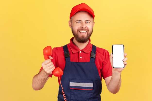 Uśmiechnięty robotnik trzymający telefon retro i telefon komórkowy z pustym ekranem dla reklamy