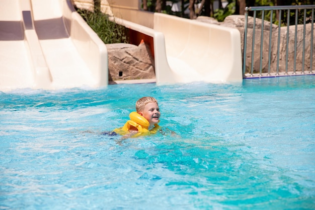 Uśmiechnięty śliczny chłopiec w dmuchanej kamizelce ratunkowej bawi się w basenie w aquaparku Concept reszta zabawy