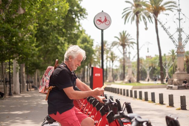 Uśmiechnięty Starszy Mężczyzna Posiadający Kartę Kredytową Wypożyczalnia Rowerów Elektrycznych W Publicznym Parku. życie W Mieście