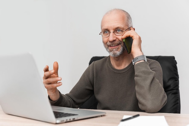 Uśmiechnięty starszy mężczyzna rozmawia przez telefon komórkowy siedząc w miejscu pracy