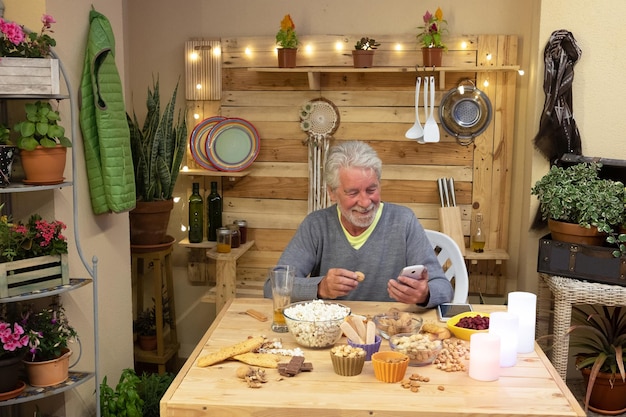 Zdjęcie uśmiechnięty starszy mężczyzna używający telefonu komórkowego podczas jedzenia jedzenia w domu
