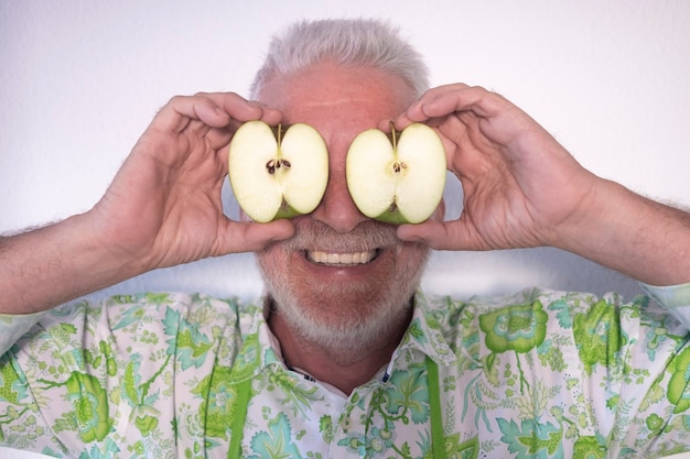Uśmiechnięty starszy mężczyzna z przeciętym na pół zielonym jabłkiem i umieszczonym przed jego oczami