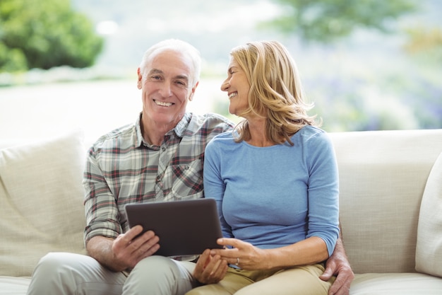 Uśmiechnięty starszy para siedzi na kanapie z cyfrowym tabletem w salonie