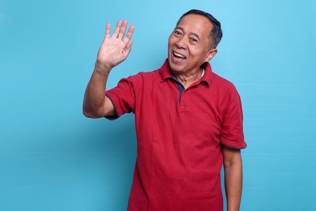 Uśmiechnięty starszy przyjazny azjatycki mężczyzna macha rękami mówiąc goobye lub Cześć odizolowany na niebieskim tle