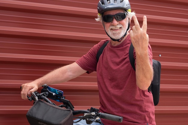 Uśmiechnięty starszy rowerzysta w miejskim mieście ze swoim elektrycznym rowerem w pobliżu czerwonego metalowego panelu