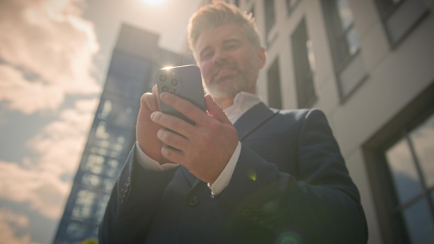 Uśmiechnięty starzec biznesmen w średnim wieku korzystający z telefonu komórkowego na zewnątrz w słońcu, szczęśliwy starszy dorosły