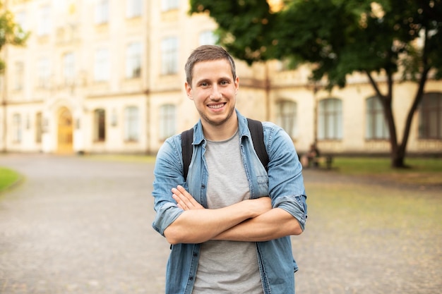 Uśmiechnięty student uniwersytetu z plecakiem spacerujący po kampusie uniwersyteckim na ulicy