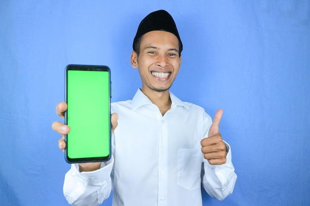 Zdjęcie uśmiechnięty szczęśliwy muzułmański azjat noszący czapkę pokazujący pusty ekran telefonu koncepcja reklamowa