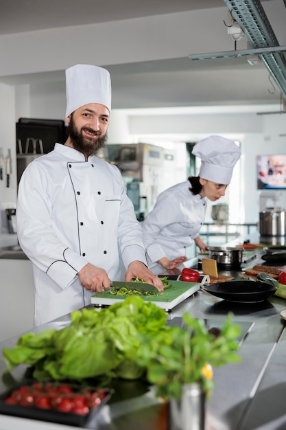 Uśmiechnięty Szef Kuchni Gotuje Dania Gastronomiczne, Przygotowując Przy Tym Dekoracje W Profesjonalnej Kuchni Restauracji. Szef Kuchni Dla Smakoszy Przygotowujący Przepis Na Danie Podczas Krojenia świeżych Warzyw.