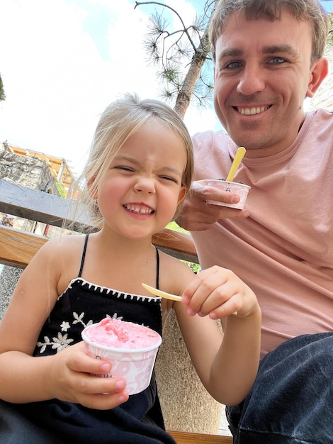 Uśmiechnięty tata z małą dziewczynką siedzi z lody w filiżankach na ławce