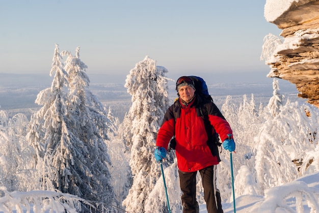 Uśmiechnięty turysta z plecakiem stojący w mroźnym zimowym krajobrazie stoi na szczycie wzgórza