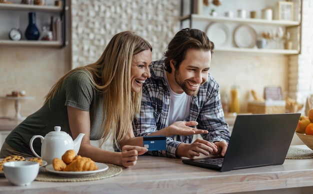 Uśmiechnięty tysiącletni mężczyzna rasy kaukaskiej z zarostem i damą z kartą kredytową robi zakupy online na laptopie