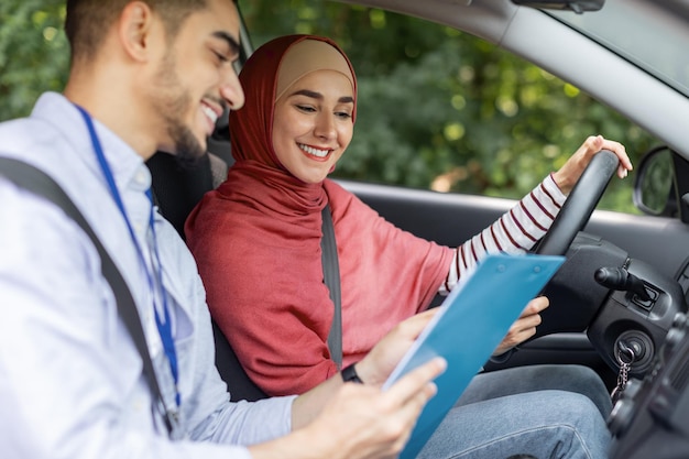 Uśmiechnięty Tysiącletni Mężczyzna Z Bliskiego Wschodu Wyjaśnia Zasady, Stawia Na Egzamin Na Prawo Jazdy Dla Kobiety W Hidżabie