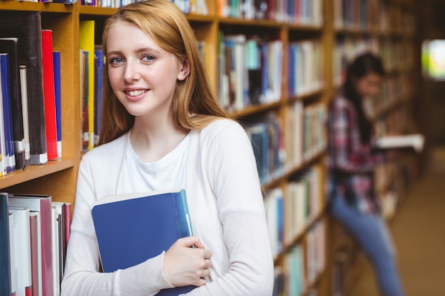 Uśmiechnięty uczeń opiera przeciw biblioteczkom