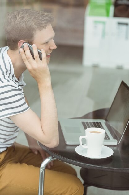 Uśmiechnięty uczeń używa laptop i smartphone w kawiarni