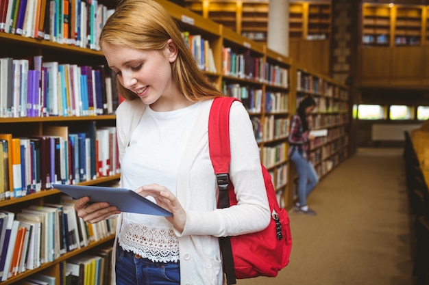 Uśmiechnięty uczeń z plecakiem używać pastylkę w bibliotece