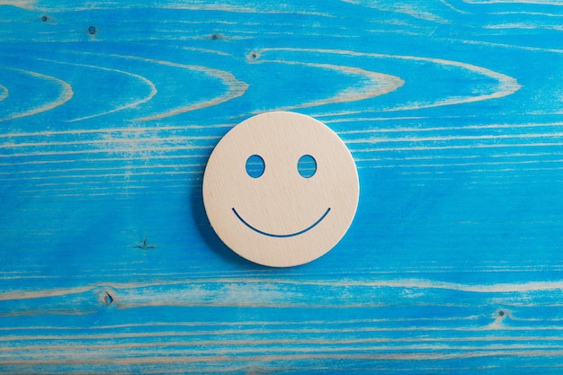 Uśmiechnięty wyraz twarzy wycięty w drewniany okrąg umieszczony na niebieskim tle