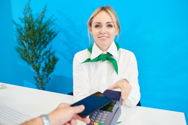 Zdjęcie uśmiechnięty żeński bank kierownik w szalika mienia terminal dla płatników