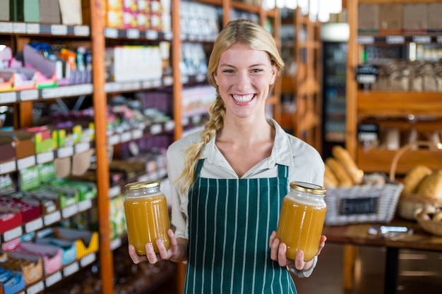 Uśmiechnięty żeńskiego personelu mienia słoje miód w supermarkecie