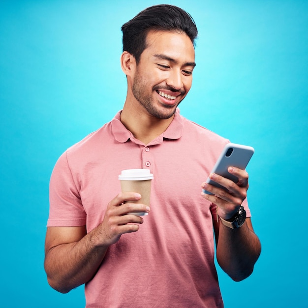 Uśmiechnij się do kawy i mężczyzny z telefonem w studio odizolowanym na niebieskim tle Herbaciany telefon komórkowy i szczęście azjatyckiej osoby z napojem kofeinowym i telefonem komórkowym do pisania w mediach społecznościowych lub wysyłania SMS-ów