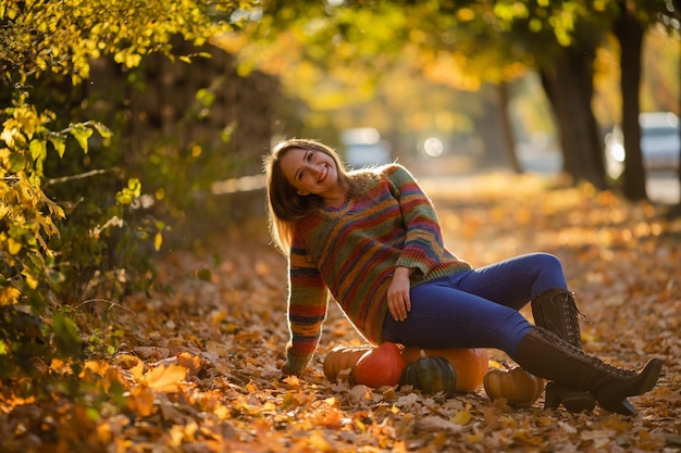 Uśmiechnij się kobiety siedzącej na dyni na jesiennych liściach klonu