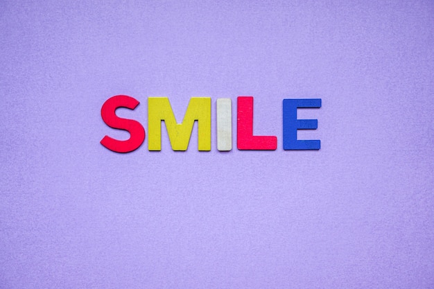 Uśmiechnij się słowo z drewnianymi literami na fioletowym tle