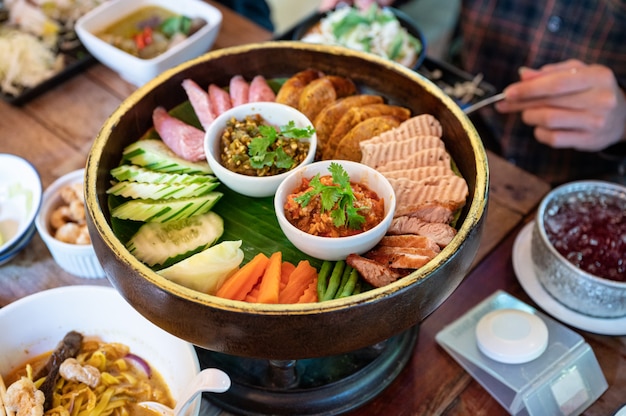 Ustaw przystawkę z północnotajlandzkiego jedzenia ze smażoną wieprzowiną, kiełbasą, warzywami i dipem z tajskiego sosu chili na Khantoke lub tradycyjnym pojemniku