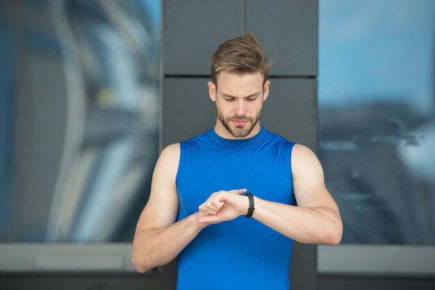 Ustaw trasę. Mężczyzna sportowiec zajęty twarz sprawdzić fitness tracker tła miejskiego. Sportowiec z włosiem patrzy na monitor fitness lub krokomierz. Trening sportowca z gadżetem krokomierza. Koncepcja gadżetu sportowego.