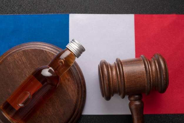 Ustawodawstwo alkoholowe we Francji Butelka alkoholu i drewniany młotek jako symbol prawa na tle flagi Francji