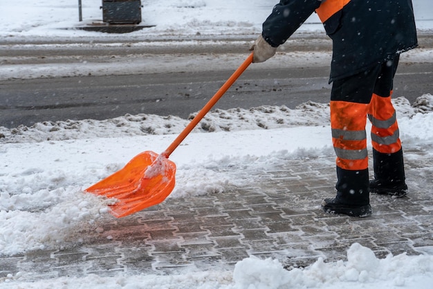 Usuwanie śniegu z chodnika po śnieżycy Drogowiec z łopatą w rękach i w specjalnym ubraniu czyści chodnik i drogę ze śniegu Śnieżyca i huragan w mieście