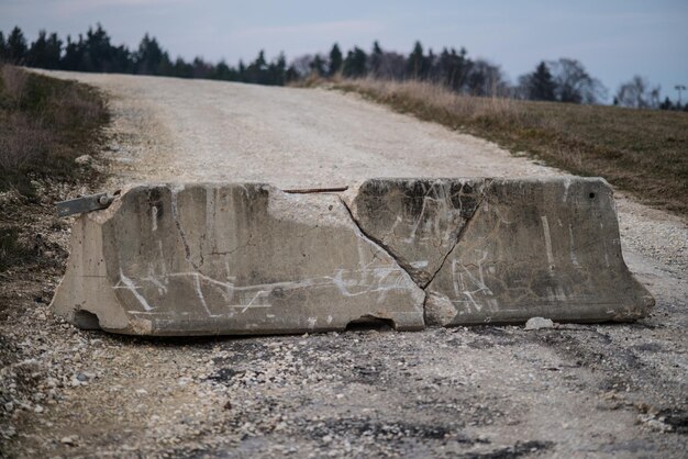 Zdjęcie uszkodzona betonowa barykada na brudnej drodze.