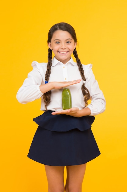 Utrzymuję energię. Szczęśliwy energiczny uczeń trzymając butelkę soku na żółtym tle. Mała dziewczynka z warkoczami z długimi włosami czuje się zdrowa z napojem energetycznym. Inteligentny i energiczny.