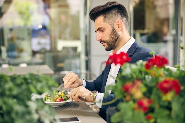 Uważny brodaty mężczyzna siedzący w pół pozycji i patrzący na kolorowe warzywa na talerzu