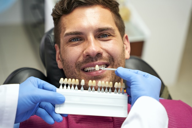 Uważny dentysta dobierający odpowiedni kolor szkliwa zębów