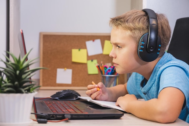 Zdjęcie uważny uczeń w słuchawkach studiuje w domu z laptopem nauka w domu