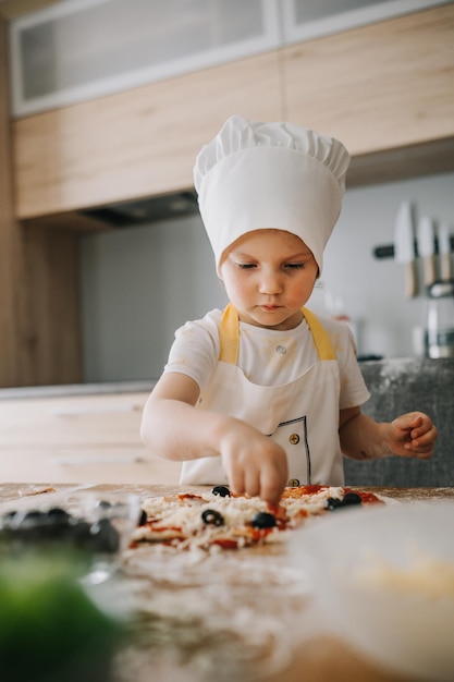 Uwielbiana szczęśliwa dziewczyna w szefowym kapeluszu i fartuchu gotuje pizzę w kuchni