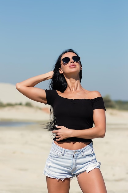 Uwodzicielska ładna kobieta w czarnej bluzce i czarnych majtkach, stojąca na piaszczystej plaży i patrząca w kamerę