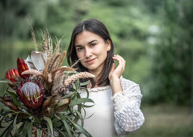 Uwodzicielska Młoda Brunetka Kobieta W Białej Sukni Z Bukietem Kwiatów W Lesie Na Rozmytym Tle