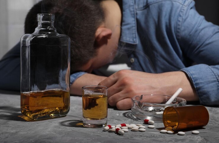 Zdjęcie uzależnienie od alkoholu i narkotyków człowiek z whisky, palący papierosy i pigułki przy szarym stole z teksturą, selektywne skupienie