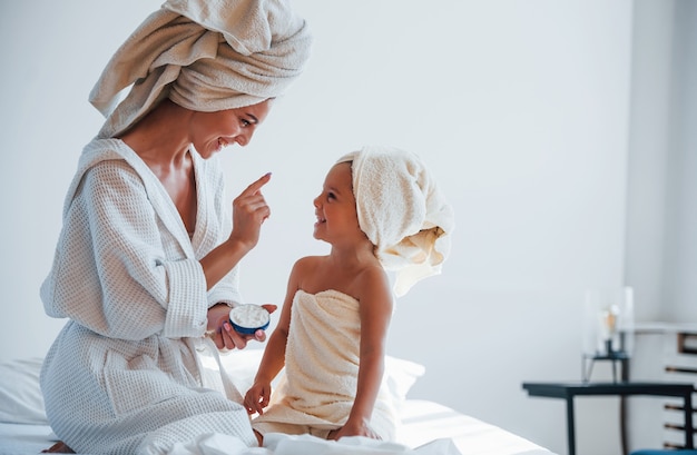 Użyj kremu do oczyszczenia skóry. Młoda matka z córką mają dzień urody w pomieszczeniu w białym pokoju.