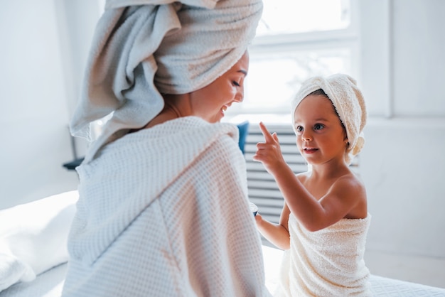 Użyj Kremu Do Oczyszczenia Skóry. Młoda Matka Z Córką Mają Dzień Urody W Pomieszczeniu W Białym Pokoju.