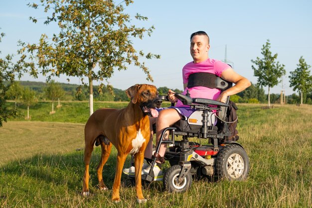 Zdjęcie użytkownik wózka inwalidzkiego z niepełnosprawnością i ich pies pomocniczy cieszący się ogrodem