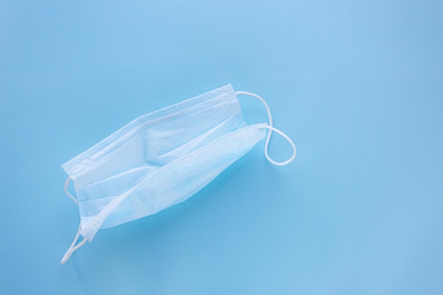 Zdjęcie używana maska medyczna z gumowymi paskami na uszy na niebieskim tle ochrona przed wirusami i bakteriami